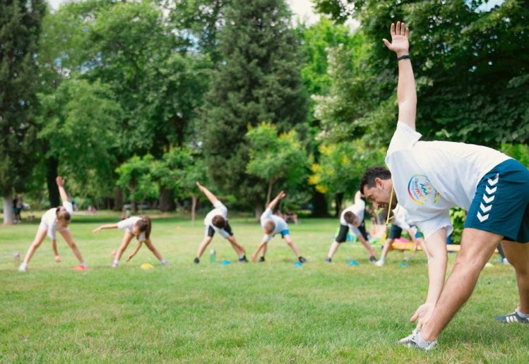 Kids stretching exercises in a park guided by a coach, promoting fitness and fun.