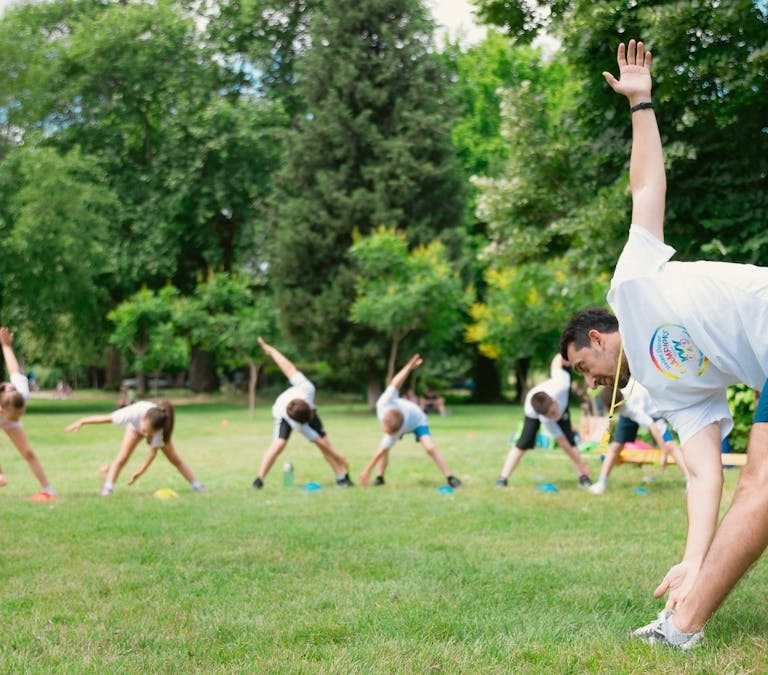 Kids stretching exercises in a park guided by a coach, promoting fitness and fun.